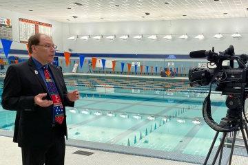 Professor Paul MacArthur stands next to the UC Pool discussing the Olympics.